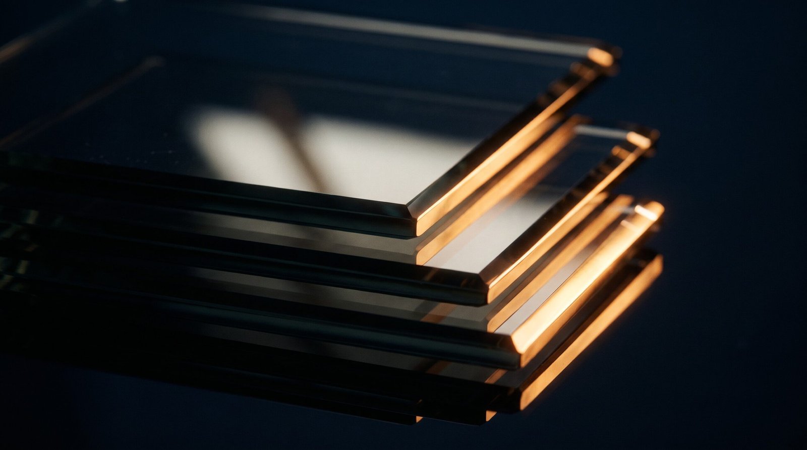 Panes of dark glass stacked at slight offsets, their edges catching a warm amber light.